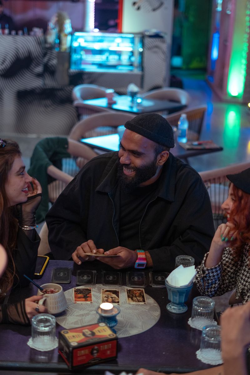 A group of friends sitting around a table with phones showing a shared expense tracking app.